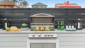 Un barbecue avec des légumes et un poulet entier, entouré d’une clôture et avec des maisons en arrière-plan.
