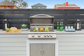 Un barbecue avec des légumes et un poulet entier, entouré d’une clôture et avec des maisons en arrière-plan.