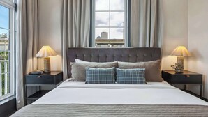 Une chambre d’hôtel avec un grand lit, deux tables de chevet, une fenêtre avec des rideaux et une vue sur le paysage urbain.