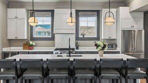 Une cuisine moderne dotée d’un îlot central, de meubles blancs et d’un éclairage suspendu.