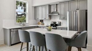 Une cuisine moderne avec des meubles gris, des appareils en acier inoxydable et un plan de travail blanc.