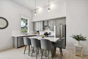 A modern kitchen with a central island, bar stools, stainless steel appliances, and a window providing natural light.