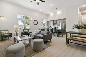 A modern living room with a sofa, ottomans, and a coffee table. There is a kitchen area with a dining table and chairs.