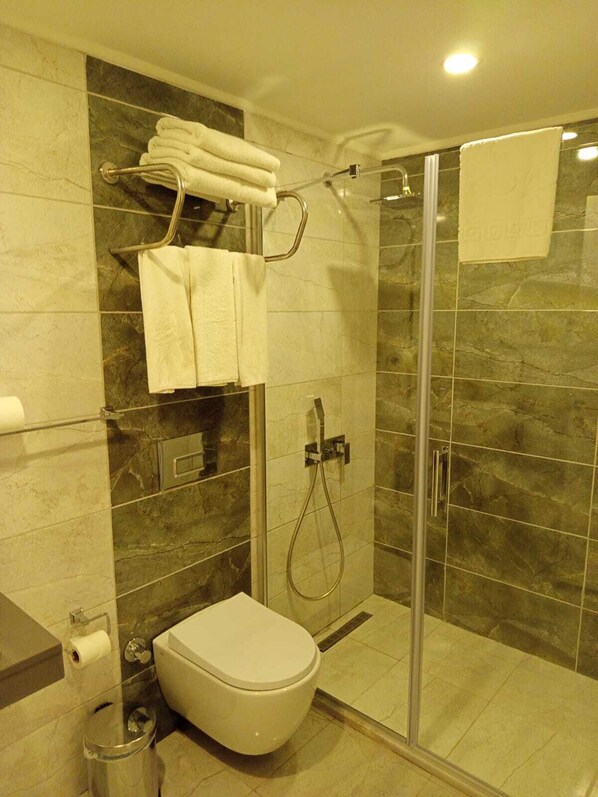 A modern bathroom with a glass-enclosed shower, a toilet, and a towel rack with folded towels. - Ber Mai Inci Hotel (Antalya)