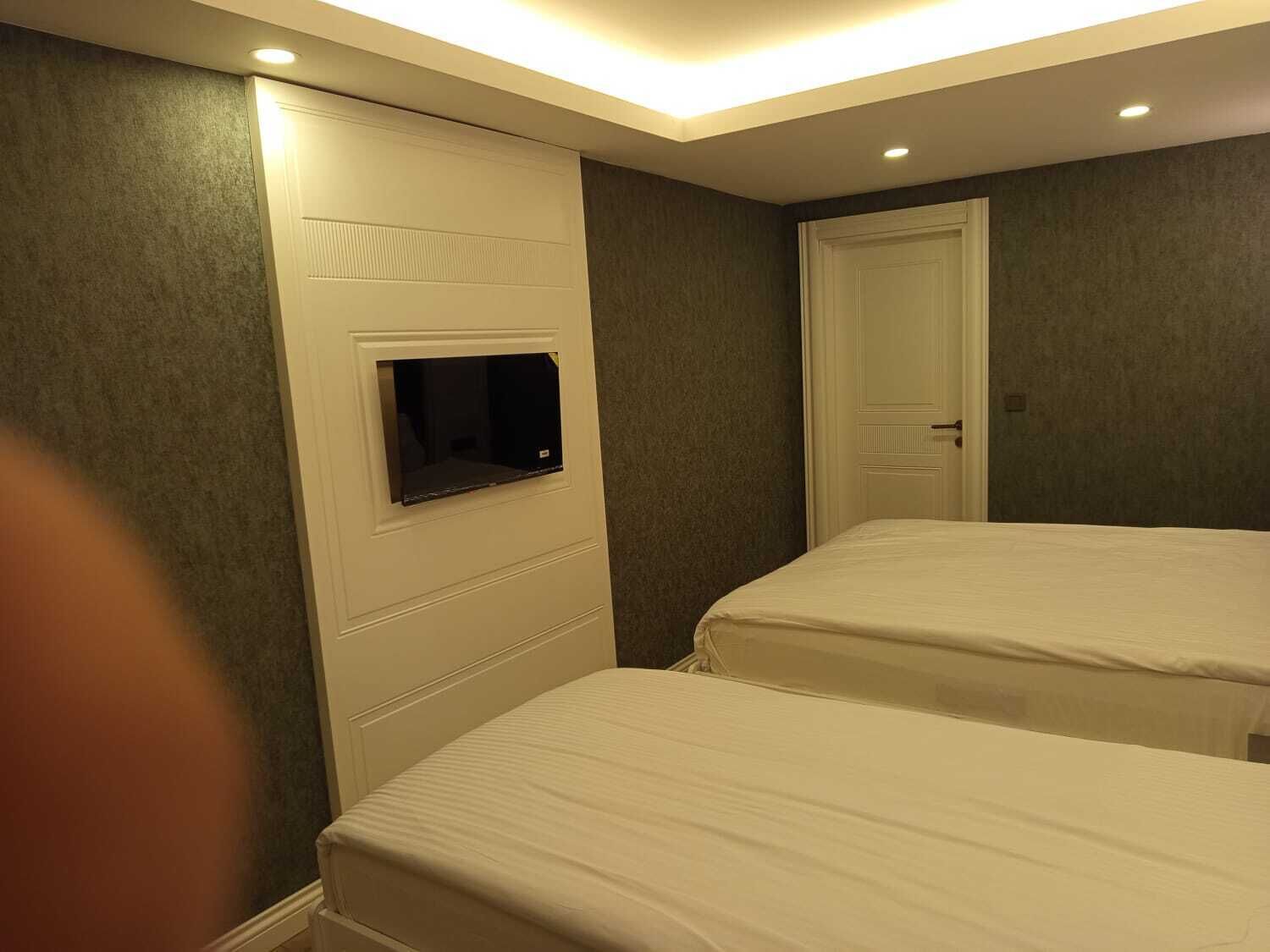 A hotel room with two single beds, a television mounted on the wall, and a door.