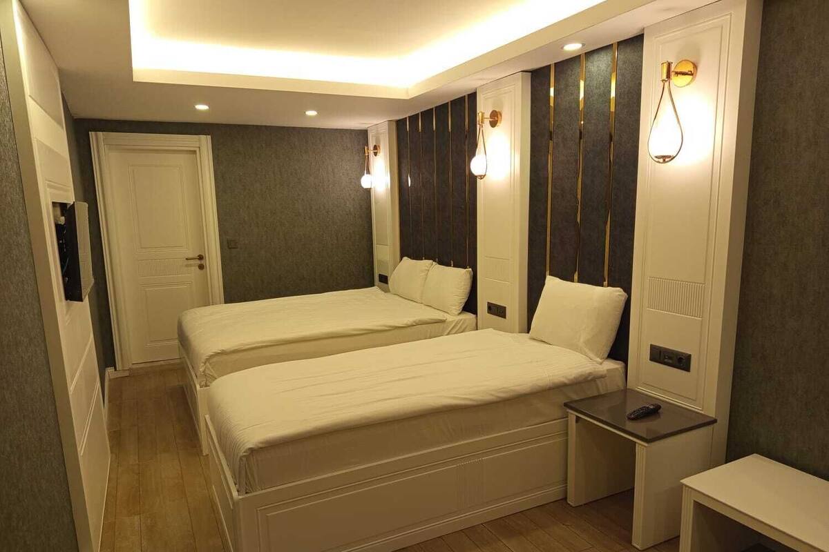 A hotel room with two beds, a bedside table, a bench, and a door.