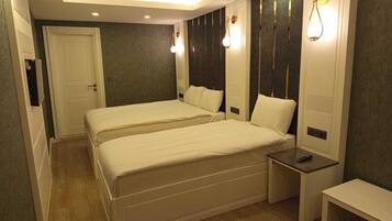 Quarto de hotel com duas camas, uma mesa de cabeceira, um banco e uma porta.