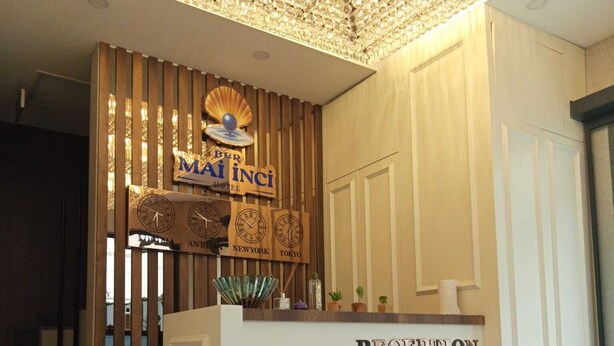 Un comptoir d’accueil avec une horloge, une enseigne indiquant « MAi inci HOTEL » et un lustre au-dessus.