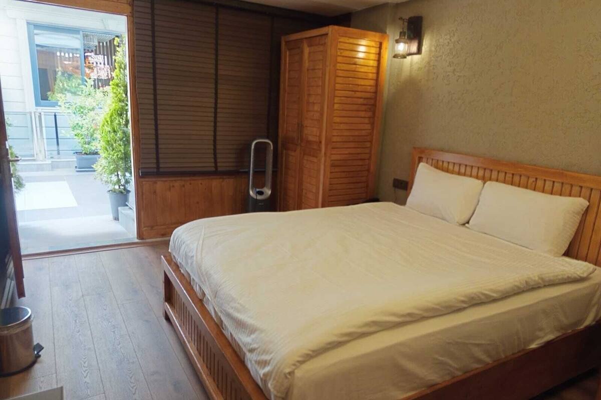 A bedroom with a wooden bed, a wooden wardrobe, and a sliding door leading to an outdoor area with potted plants.