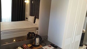 Une chambre d’hôtel comprenant un lit, une petite kitchenette, un bureau avec une bouilloire, des tasses et une télécommande.
