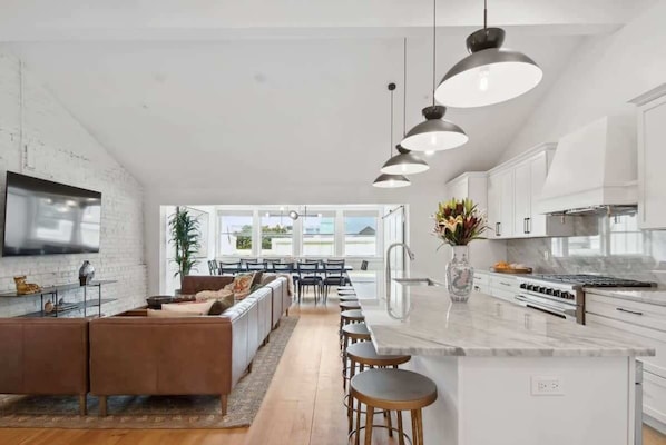 Une cuisine moderne dotée d’un grand îlot central, de luminaires suspendus et offrant une vue sur l’espace repas.