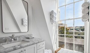 A modern bathroom with a large mirror, marble countertop, and a view of the city through a large window.