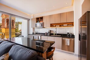 Una cocina moderna con una isla central, electrodomésticos de acero inoxidable y vistas a un balcón con un paisaje urbano.