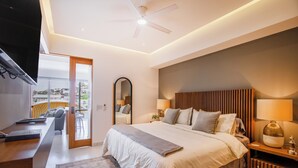 A modern bedroom with a large bed, bedside tables, a ceiling fan, and a view of the city through a glass door.