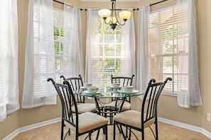 A dining area with a glass table, four chairs, and a chandelier.