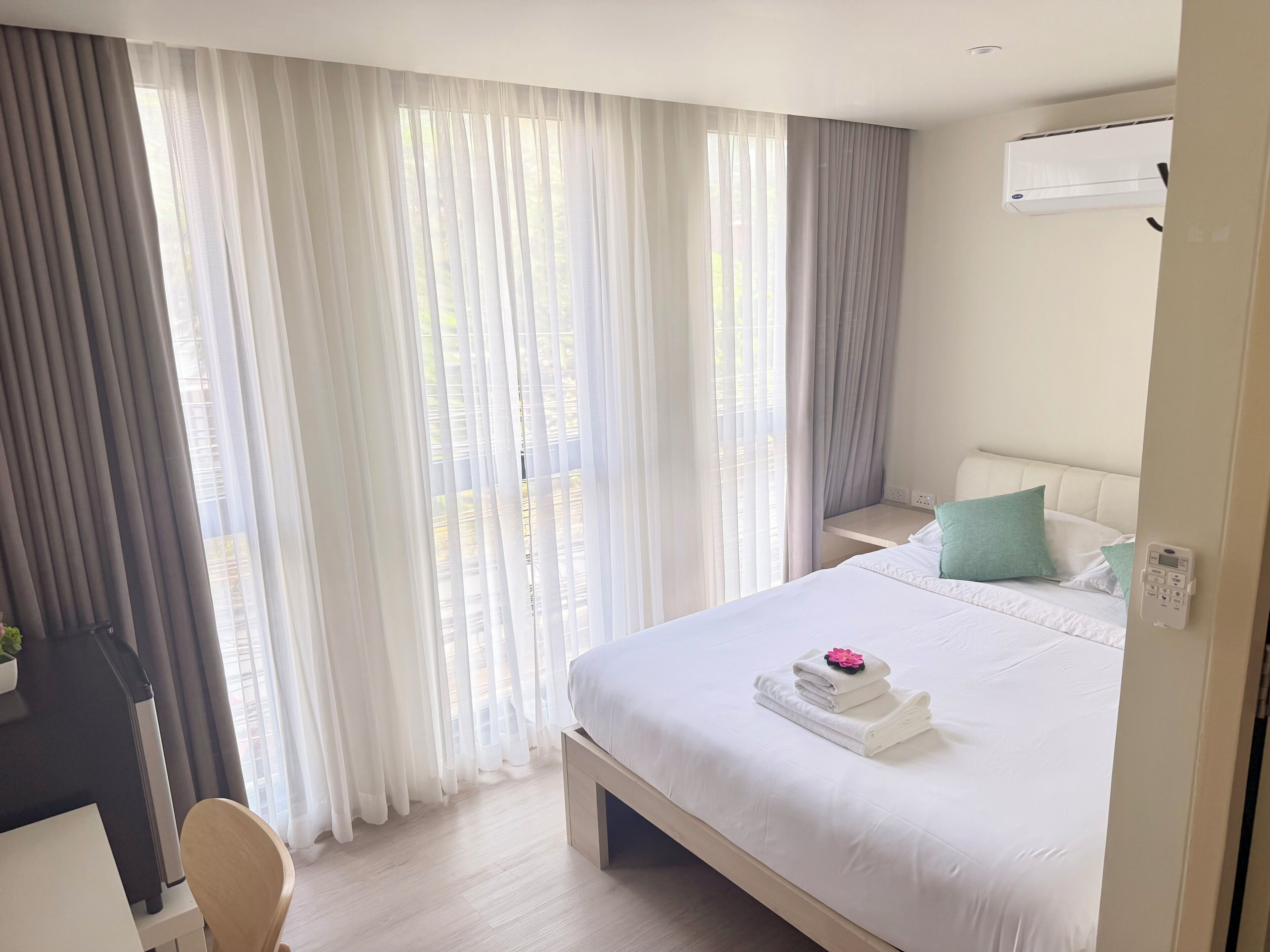 Una habitación de hotel con cama, escritorio, silla, mesita de noche y aire acondicionado.