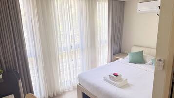 Una habitación de hotel con cama, escritorio, silla, mesita de noche y aire acondicionado.