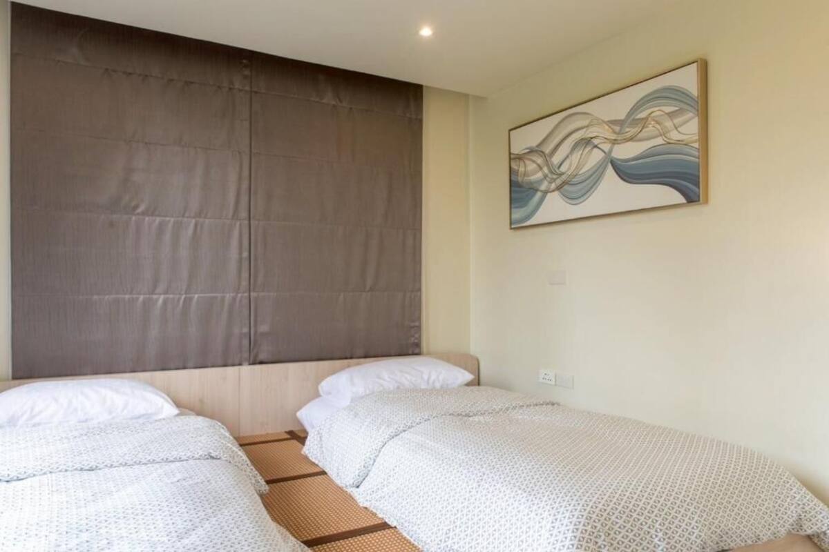 A room with two beds, a large window with a curtain, and a wall-mounted abstract painting.