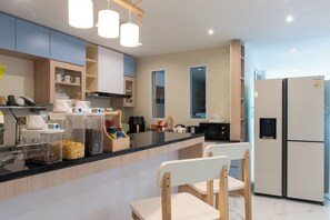 A modern kitchen with a central island, wooden chairs, and a large refrigerator. - Shizuka House (Bangkok)