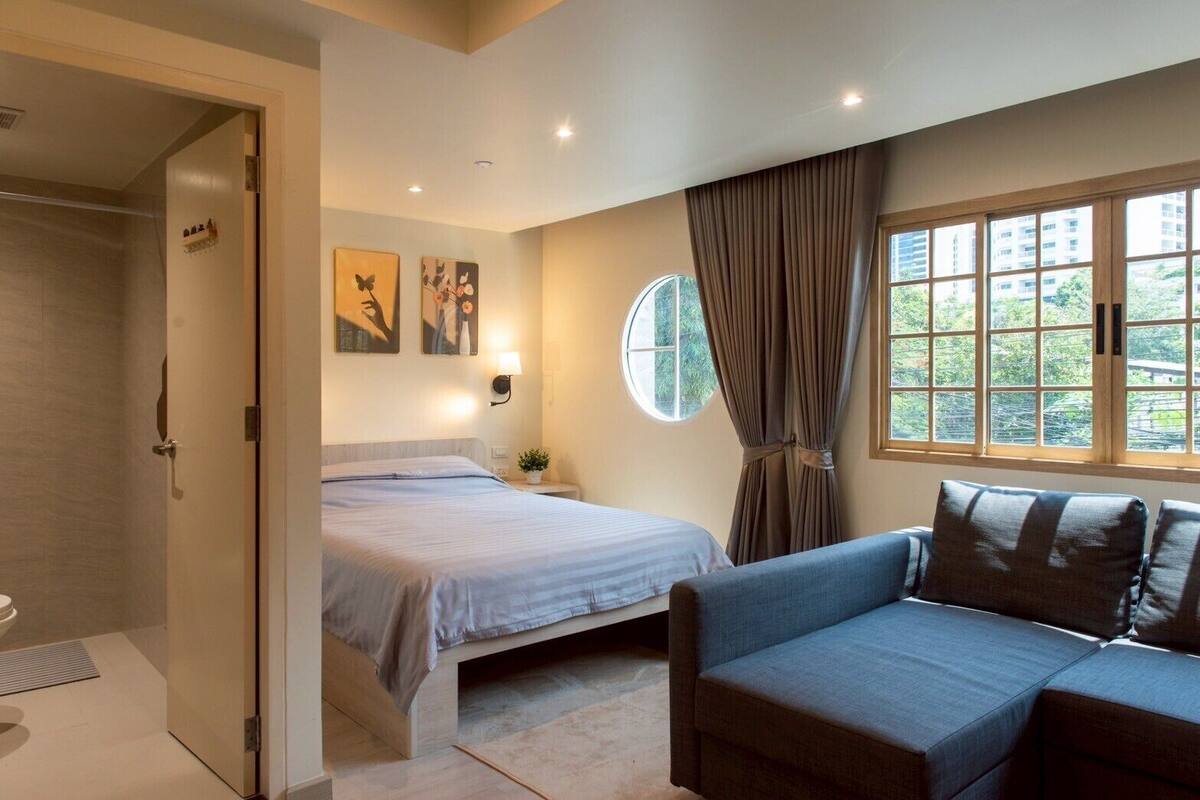 A modern hotel room with a bed, a sofa, a window with curtains, and artwork on the wall.