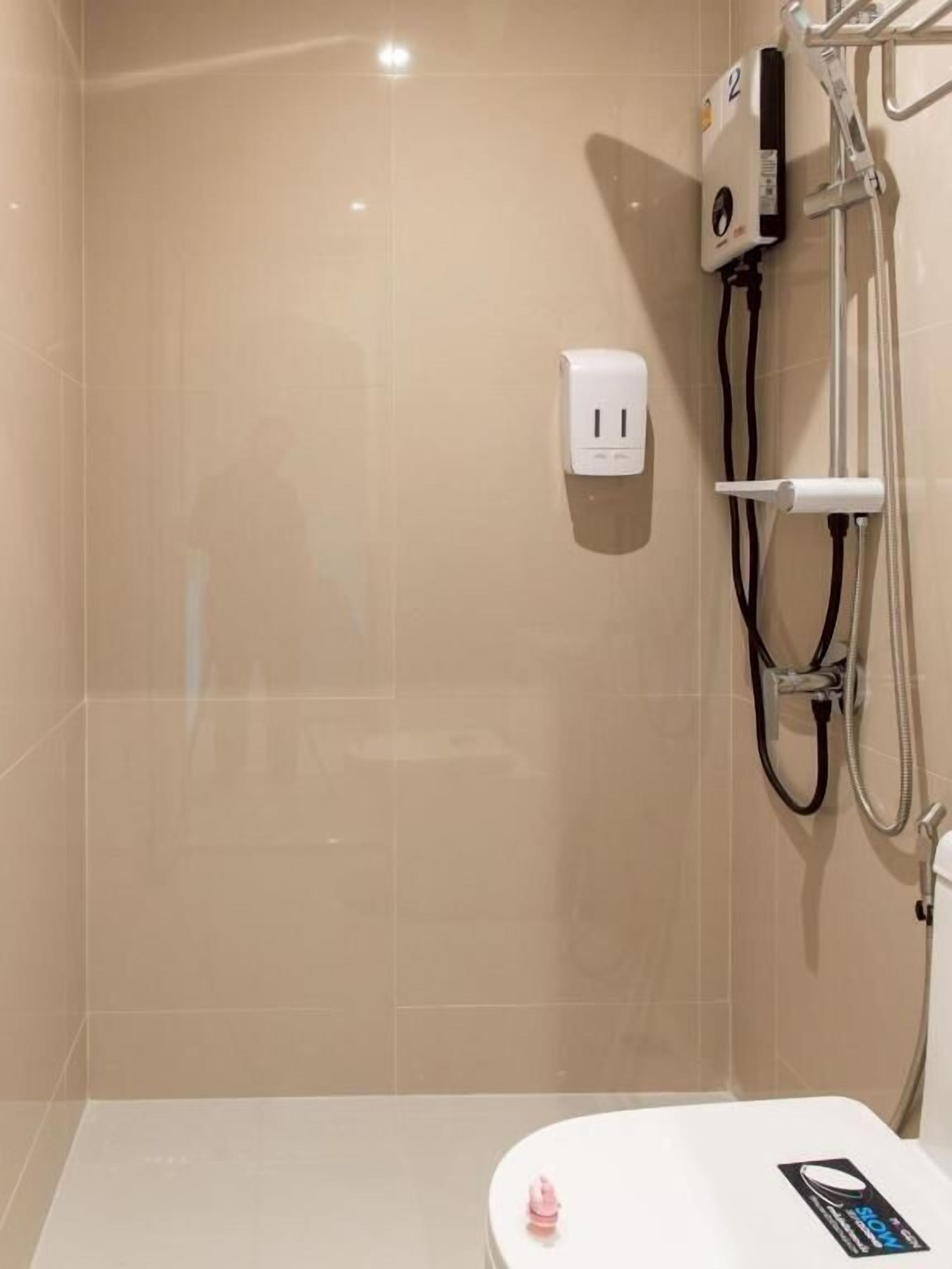 A bathroom with a toilet, a hand dryer, and a shower head.