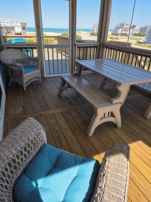 A covered outdoor area with wicker furniture, a picnic table, and a view of the beach and ocean.
