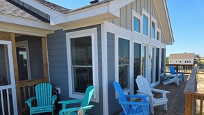 Una terraza de madera con sillas Adirondack, un porche cubierto y vista a la playa.