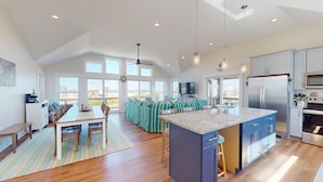 Una cocina amplia con una isla grande, un comedor con vistas y un salón con balcón con vistas a la playa.