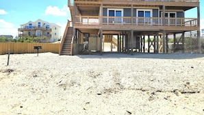 Una casa frente al mar de varios pisos con una terraza de madera y una escalera que lleva a los niveles superiores.