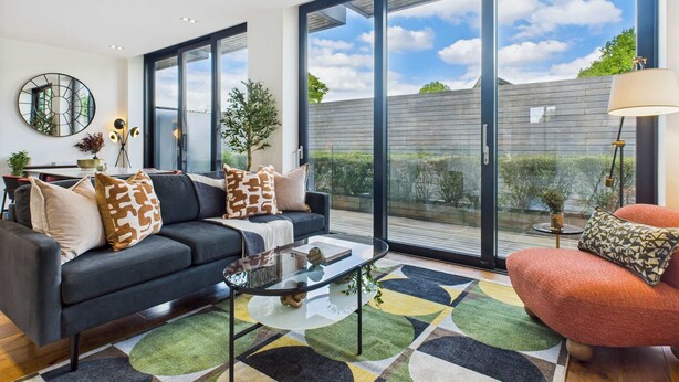 A modern living room with a sofa, coffee table, and a view of the outdoors through large windows.