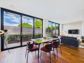 A modern living room with a glass dining area, a sofa, and a TV. - Bright Camden Town Apartment with Balcony (Greater London)