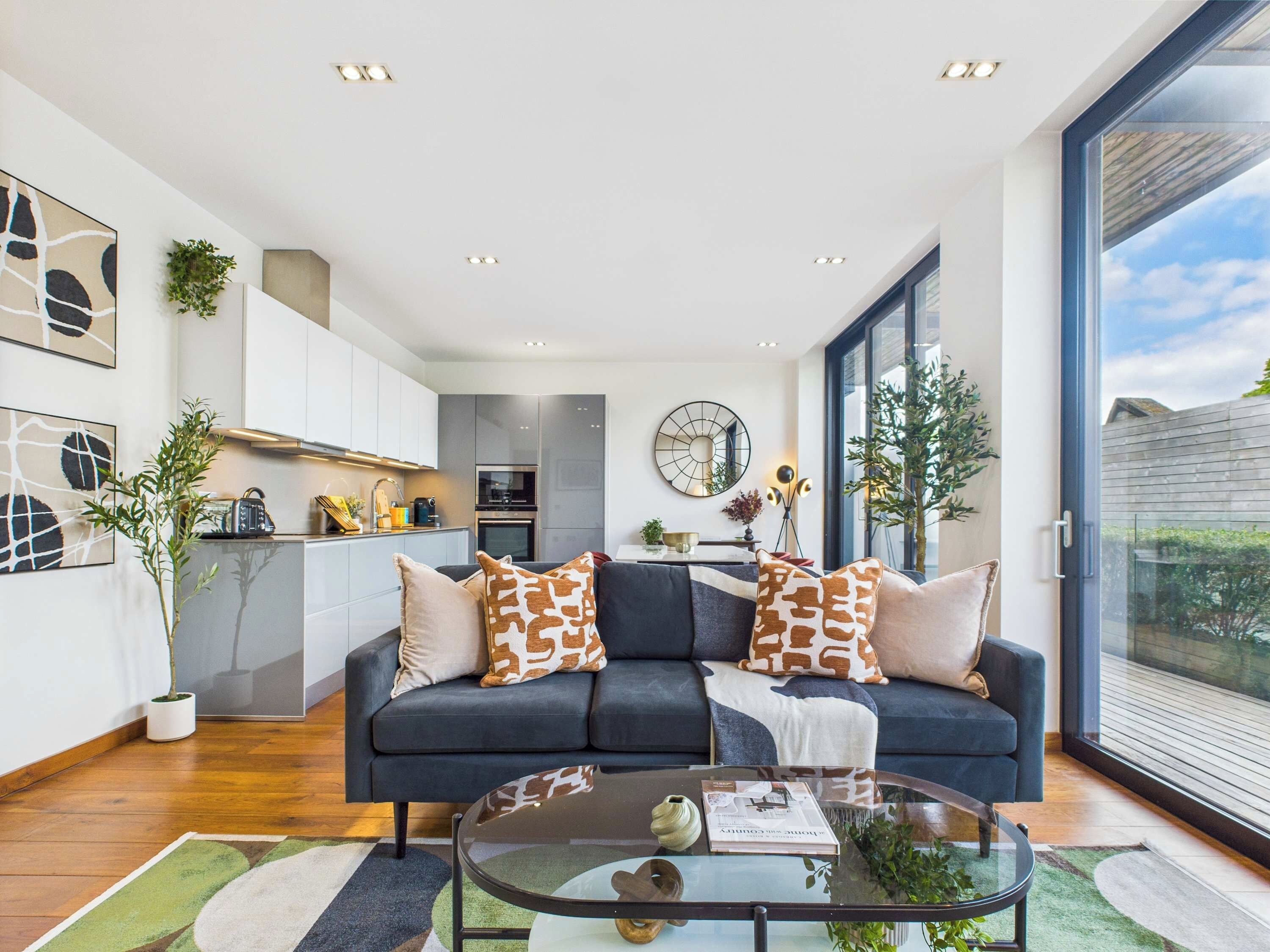 Un salon moderne avec un canapé foncé, une table basse en verre et une vue sur l’extérieur.