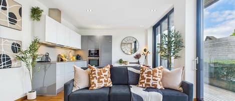 Un salon moderne avec un canapé foncé, une table basse en verre et une vue sur l’extérieur.