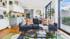 A modern living room with a dark sofa, glass coffee table, and a view of the outside.