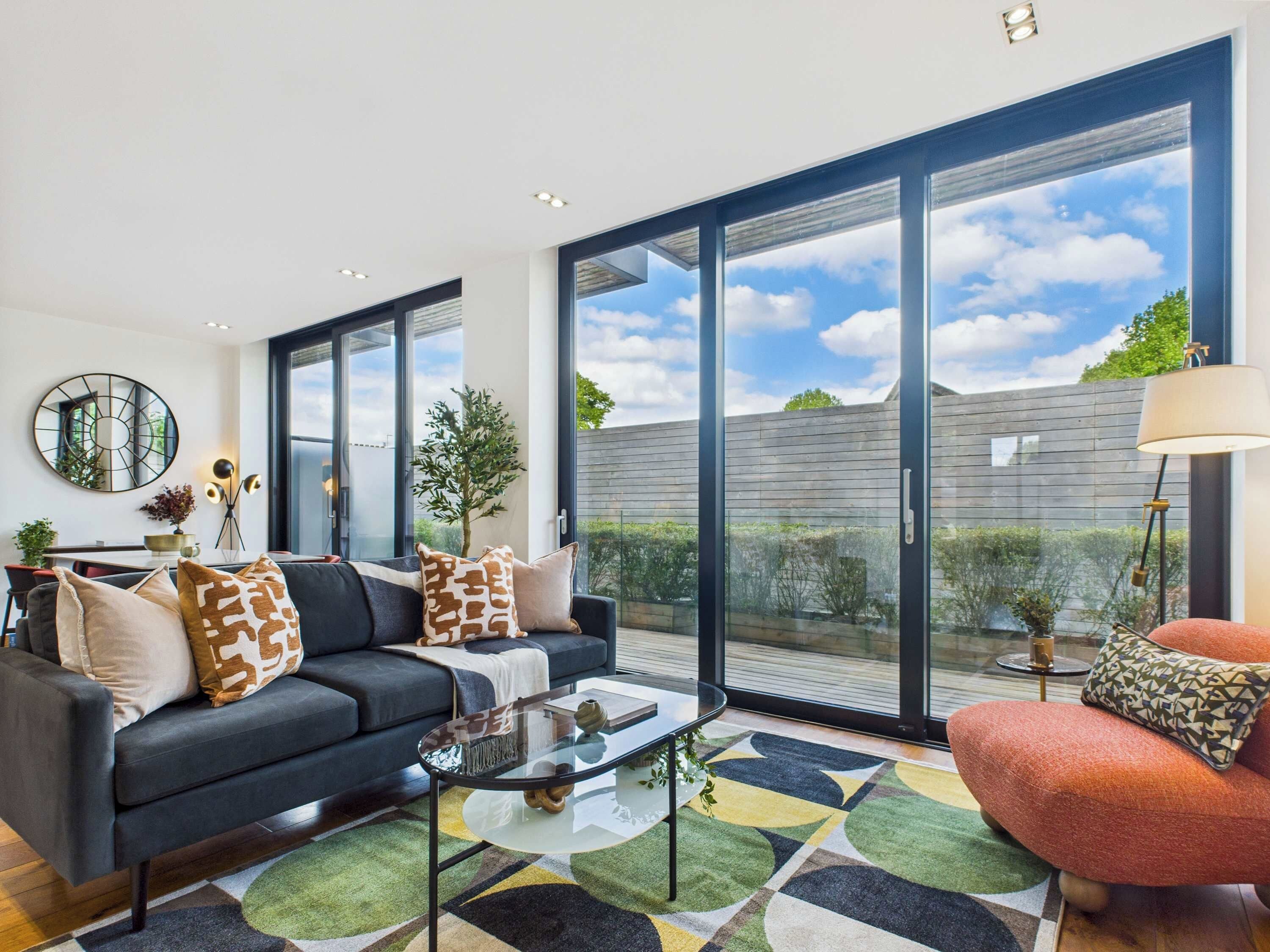 A modern living room with a sofa, coffee table, and a view of the outdoors through large windows.