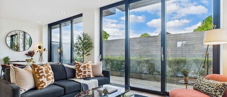 Una sala de estar moderna con un sofá, una mesa de centro y vistas al exterior a través de grandes ventanales.