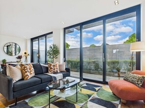 A modern living room with a sofa, coffee table, and a view of the outdoors through large windows.
