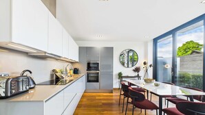 A modern kitchen with a central island, built-in appliances, and a dining area with red chairs.