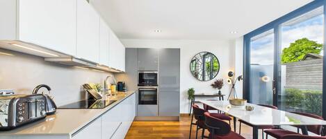 A modern kitchen with a central island, built-in appliances, and a dining area with red chairs.