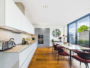 A modern kitchen with a central island, built-in appliances, and a dining area with red chairs. - Bright Camden Town Apartment with Balcony (Greater London)