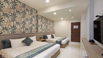 A hotel room with two beds, a large floral-patterned headboard, a small bedside table with a plant, and a TV on the right.