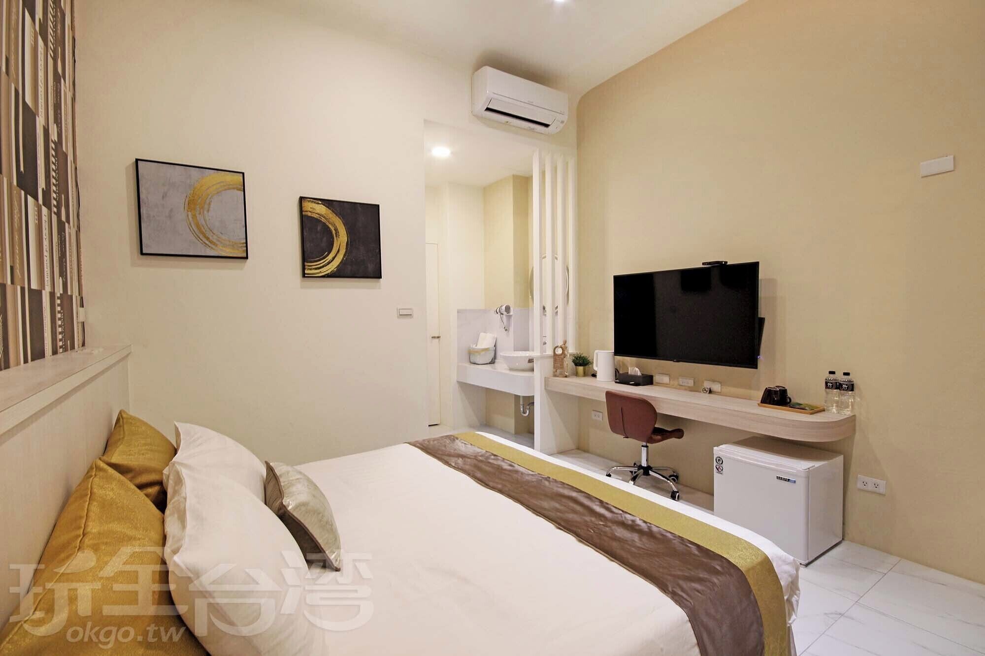 Een hotelkamer met een bed, een bureau met een televisie, een kleine koelkast en een badkamer met een wastafel en spiegel.