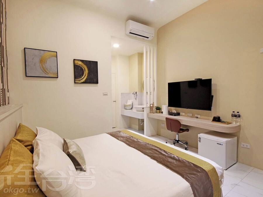 Een hotelkamer met een bed, een bureau met een televisie, een kleine koelkast en een badkamer met een wastafel en spiegel.