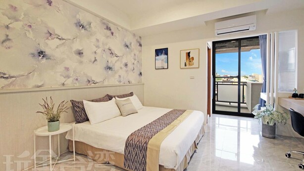 Un dormitorio con cama, mesita de noche con planta, ventana grande y balcón con vistas.