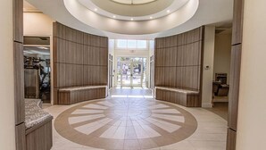 A spacious lobby with a central circular floor design, wooden paneling on the walls, and a glass ceiling.