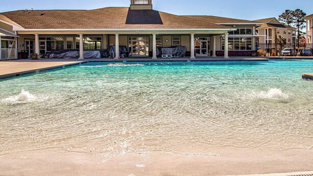 A swimming pool with clear water, a covered seating area, and a building with a sloped roof.