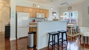 A modern kitchen with wooden cabinets, a white refrigerator, a microwave, and a small island with stools.