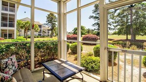 A conservatory with a table and a sofa, overlooking a landscaped garden and a golf course.