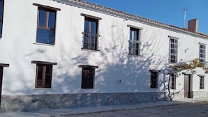 A white building with multiple windows and balconies, a stone base, and a clear sky. - El Molino De Alatoz  (Alatoz)