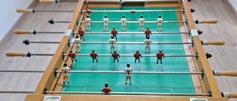A foosball table in a room with wooden flooring and a window in the background.